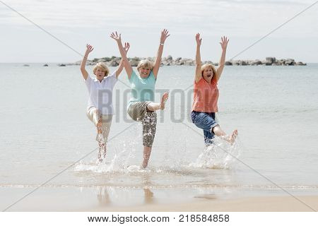 lovely group of three senior mature retired women on their 60s having fun enjoying together happy walking on the beach smiling playful in female friendship and girlfriends on holidays concept