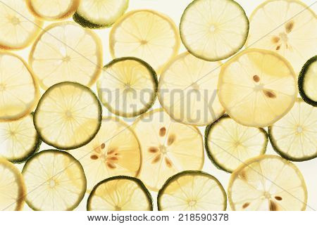 Backlit lemon and lime slices. Abstract exotic background, closeup texture of cut tropical fuits. Healthy eating, vitamins and veggie concept, top view