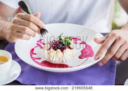 Male hands with fork and white berry meringue cake