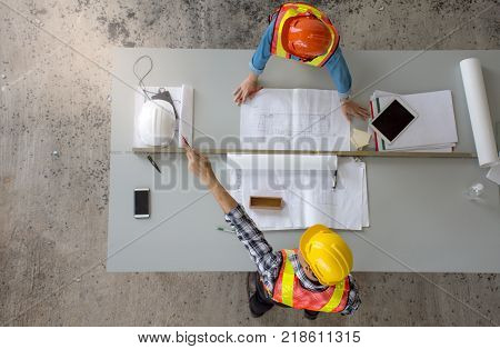 Top view of group of professional engineering team wearing safety helmet is meeting and pointing finger up , planning construction work, looking paper plans at construction site, overhead view,Concept for team work
