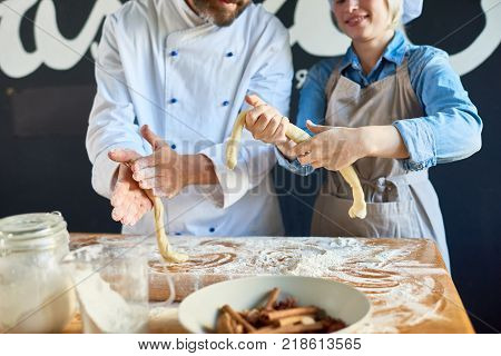 Mid-section portrait of two cheerful cooks knedding and rolling batter making Christmas pastry in restaurant kitchen