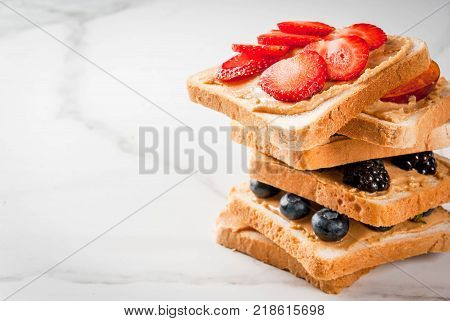 Traditional American and European summer breakfast: sandwiches of toast with peanut butter berry fruit apple peach blueberry blueberry strawberry banana. White marble table. copy space
