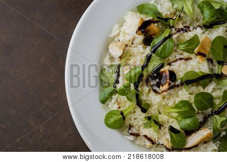 chicken and rice with valeriana salad and balsamic vinegar in a plate on wooden table