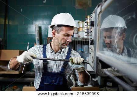 Contemporary factory technician with handtool repairing one of industrial machines