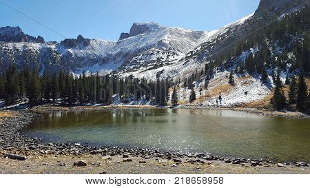 tree-ringed, clear, sparkling lake in front of snowy mountains