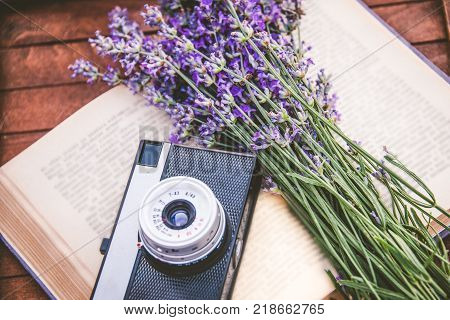 Freshly cutted lavender flowers and a vintage photo camera over an open book.Wooden background