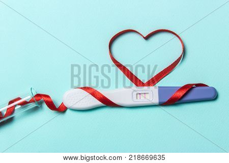 Artificial insemination a child from a test tube infertility treatment. Positive pregnancy test with two strips and a red ribbon in the form of a heart and a test-tube
