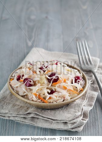 Traditional russian appetizer sauerkraut with cranberry and carrot in craft plate on gray rustic wooden table. Fermented cabbage. Russian cuisine and russian kitchen.