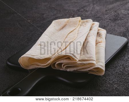 Armenian flat bread lavash. Pita bread on black cutting board over black cement background. Copy space.