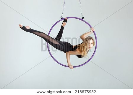 Woman aerial acrobat performs with tricks on the hula hoop at the top.