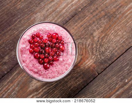 Idea for healthy breakfast on Valentine's Day: pink chia pudding with red berry puree and cranberries in shape of heart on top over wooden table background. Copy space for text Top view or flat-lay.
