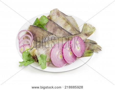 Several uncooked carcasses of the notothenia fish without of the heads cilantro twigs and round slices of red onion on a white dish on a white background