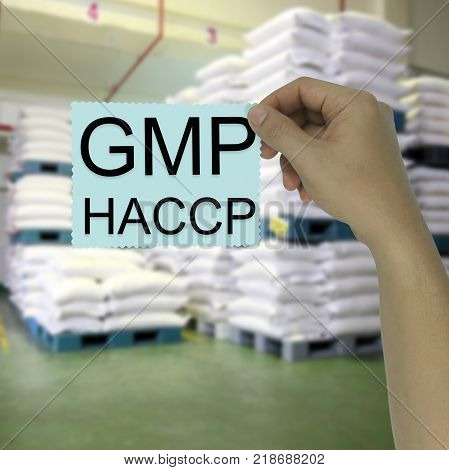 Hand of the businessman holding a paper note with GMP and HACCP text on blur warehouse background for design in your work.