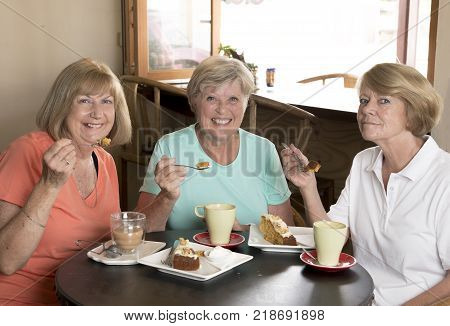 group of three lovely middle age senior mature women girlfriends meeting for coffee and tea with cakes at coffee shop sharing time together enjoying converstion happy and cheerful gossiping