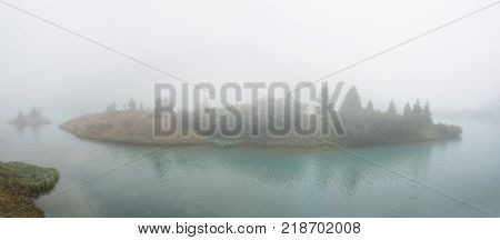 Island on a rainy and misty autumn. Wood on the ash. Alpengasthof Zeinisjoch, Zeinisjoch lake, Austria, Europe