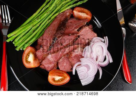 business lunch fresh roast beef meat slices on black plate wotj cutlery asparagus boiled broccoli rye bun on wooden table