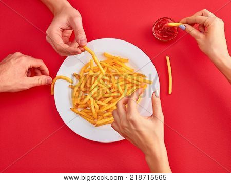 Young woman and man eating french fries potato with ketchup in a restaurant, having her lunch break. Close up