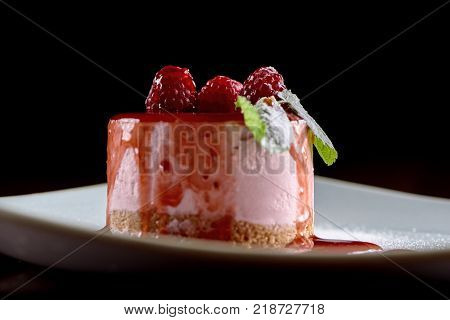 Close-uf a delicious souffle dessert decorated with raspberies and fresh mint leaves, served on white square plate. Photo was taken on black background. Tasty for sweet buffet or catering.