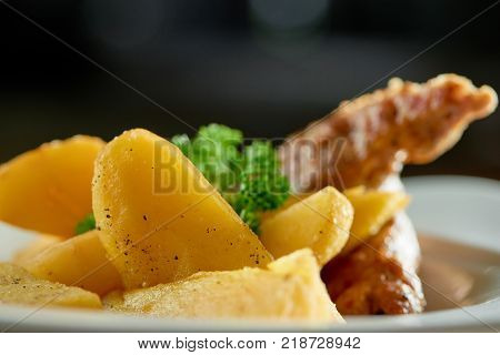 Close-up of goldy fried potatoes slices with roasted sausage and parsley on whe white plate.