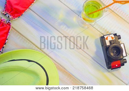Bright summer women's accessories on a colored wooden background- a vintage photo camera, a red swim suit, a green hat and a tripical cocktail. Space for a text or product display.