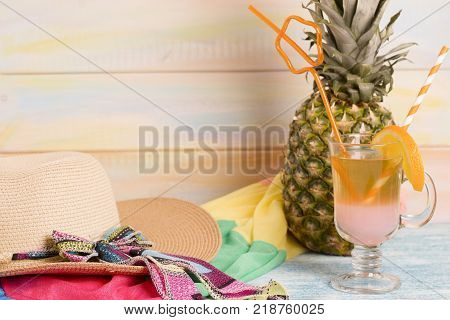 Enjoy tropic vacation with a fresh pineapple an exotic cocktail and a straw hat. Bright fabrick background. Tourism concept background, top view. Space for a text or product display.