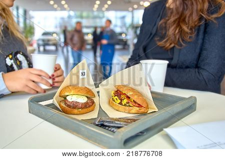 two women chatting during lunch. on a table delicious burger with fried meat cutlet, hot-dog, placed in wooden tray. In the showroom.