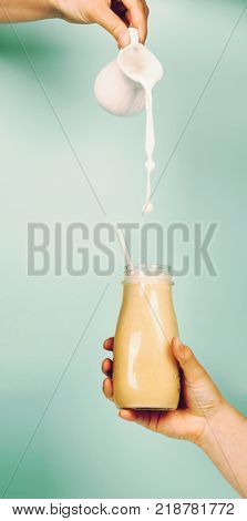 Woman (teenage girl) hand holding smoothie shake against bright wall. Pouring milk (cow or almond) into smoothie. Drinking healthy smoothie concept