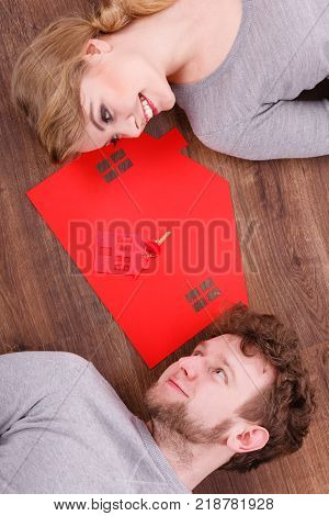 Housing marriage family security future finances mortgage concept. Just married lying on floor. Young man and woman next to home symbol with keyring.