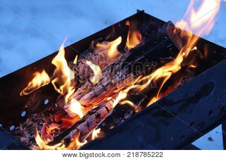 Background of fire and black wood. Dark grey black white coals on bright fire inside metal brazier. Wood burning in the brazier. Flames fire. Preparation for cooking barbecue.