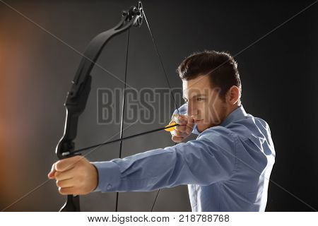 Young businessman practicing archery on dark background