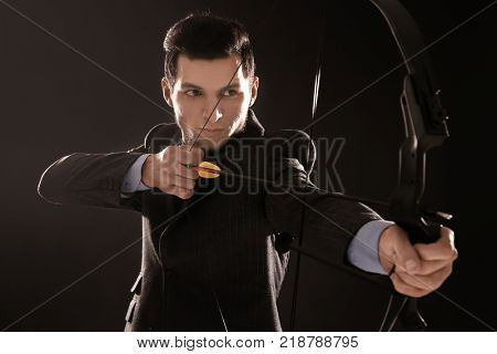 Young businessman practicing archery on dark background