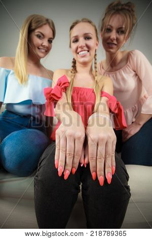 Woman showing her beautiful painted finger nails with red neon nail polish. Two female friends in background