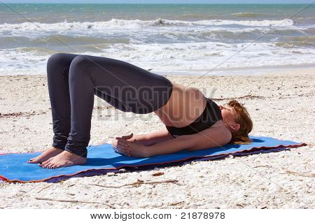Mujer joven haciendo ejercicio de Yoga en la playa en Setu Bandhasanasana o postura de puente
