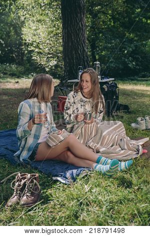 Happy young women friends laughing sitting in campsite into the forest