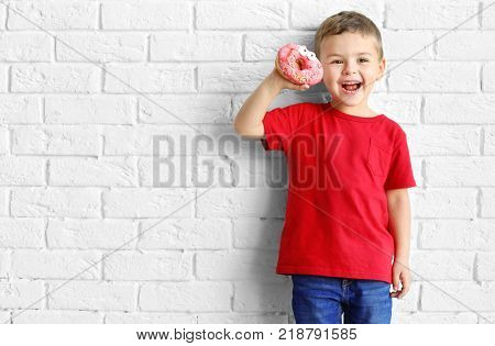 Little boy with sweet donut near white brick wall
