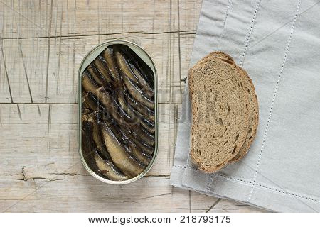 Tin can of sprats, sardines with bread pieces on wooden table. Top view and free space. Selective focus.