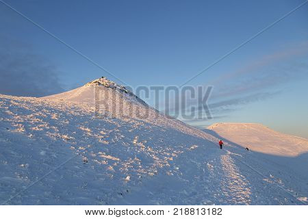 Pen y Fan, Wales, UK: December 11, 2017: A man wearing distinctive red winter clothing walks toward the camera in a winter snow scene on Pen y Fan mountain in the Brecon Beacons National Park