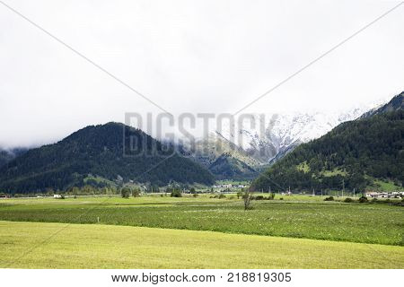 View Landscape Of Mountain And Grass Field Beside Road Near Haidepark Burgeis In Trentino-alto Adige