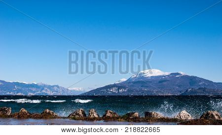 Landscape of a lake with waves and squirts on a windy day background with alpine mountains