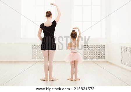 Little girl learning ballet with teacher copy space. Cute small ballerina training classical dance exercises with female coach, back view