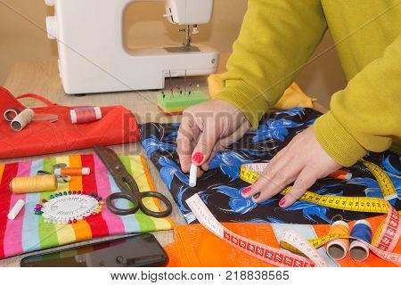 Close up of woman's hands drawing a pattern on yellow tissue. Measuring tape and sewing accessories. A tailor is laying out a dress. Sewing layout tailoring concept