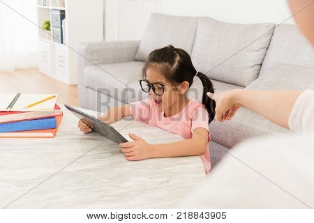 selective focus photo of mother blame little daughter using mobile pad computer playing game and school homework not finished.