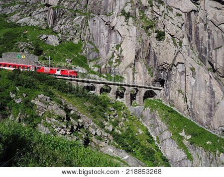 ANDERMATT, SWITZERLAND EUROPE on JULY 2017: Express St. Gotthard train on Teufelsbruecke, Devil's railway bridge and tunnel, swiss Alps, alpine rocky mountains landscape scenery in warm summer day.