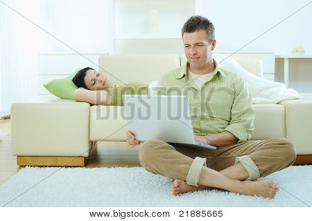 Mann sitzt am Boden zu Hause Surfen Internet auf Laptop-Computer, Woman sleeping on Sofa.?