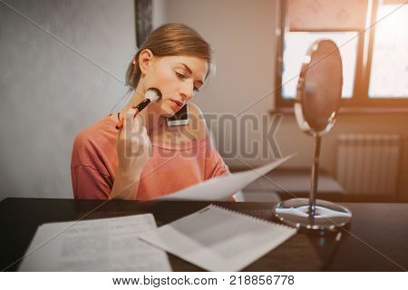 Busy woman making a make-up, talking on the phone, reading documents at the same time. Businesswoman doing multiple tasks. Multitasking business person.