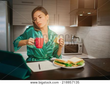 Busy woman eating, drinking coffee, talking on the phone, working on tablet at the same time. Businesswoman doing multiple tasks. Multitasking business person. Freelancer works at night.