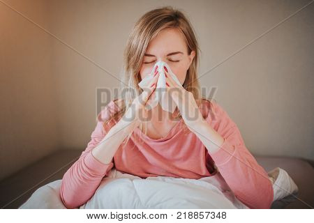 picture from a young woman with handkerchief. Sick girl has runny nose. female model makes a cure for the common cold. The patient lies in bed.