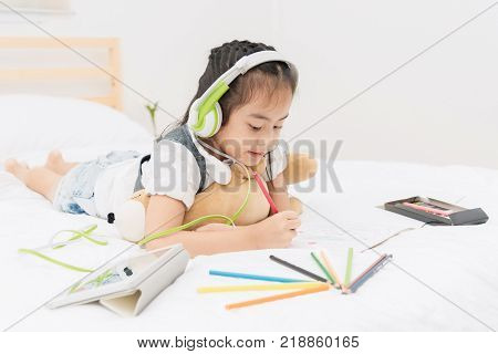 Little girl listen to music from headphone while drawing picture,relaxing and education concept.