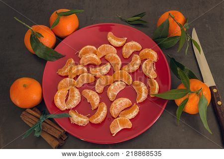 Bright juicy tangerines lie on a red plate. Cinnamon sticks tied with a green ribbon and knife are on the table.