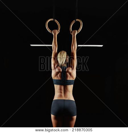 Full length rearview shot of a female athlete performing pull-ups on gymnastic rings. Fitness woman with strong beautiful body exercising on gym rings health power endurance competitive